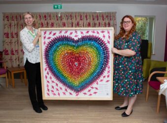 2 females holding a large heart art work