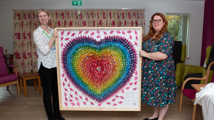 2 females holding a large heart art work